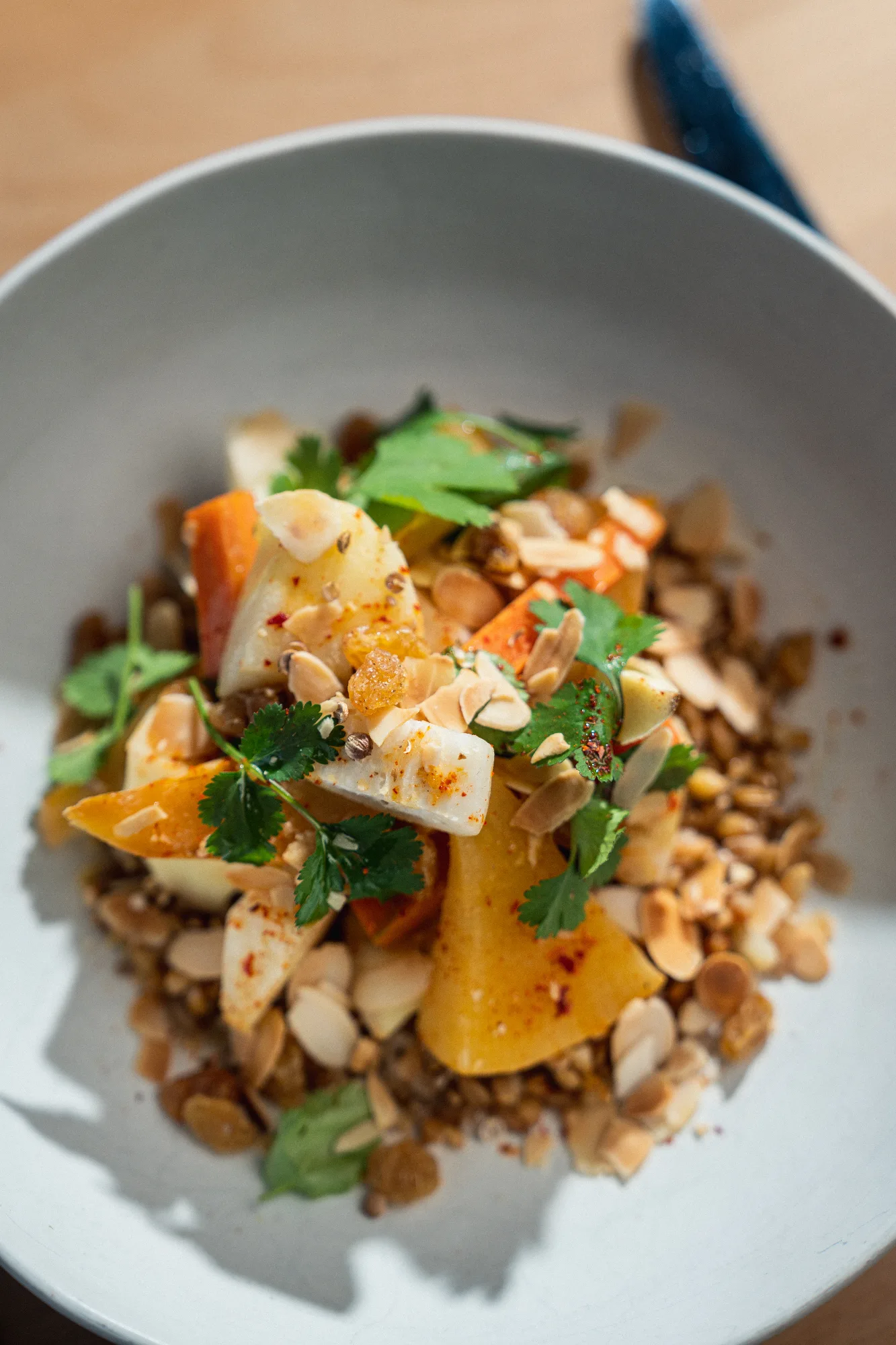 Assiette creuse blanche garnie de lentilles, légumes rôtis dorés, amandes effilées et coriandre fraîche, dressée avec soin pour la bistronomie d'HABILE.