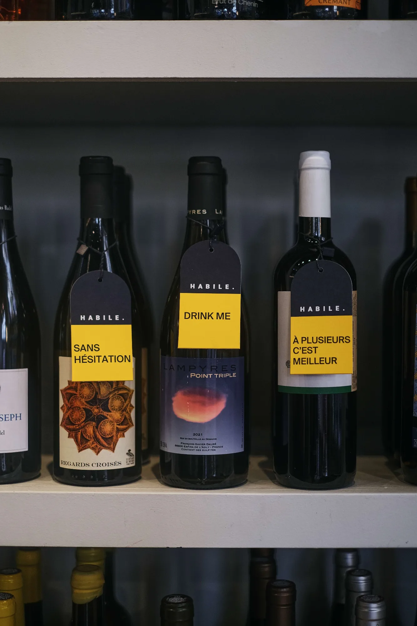 Étagères de la cave d'HABILE. garnies de bouteilles de vins vivants, chacune accompagnée d'une étiquette jaune manuscrite - zoom