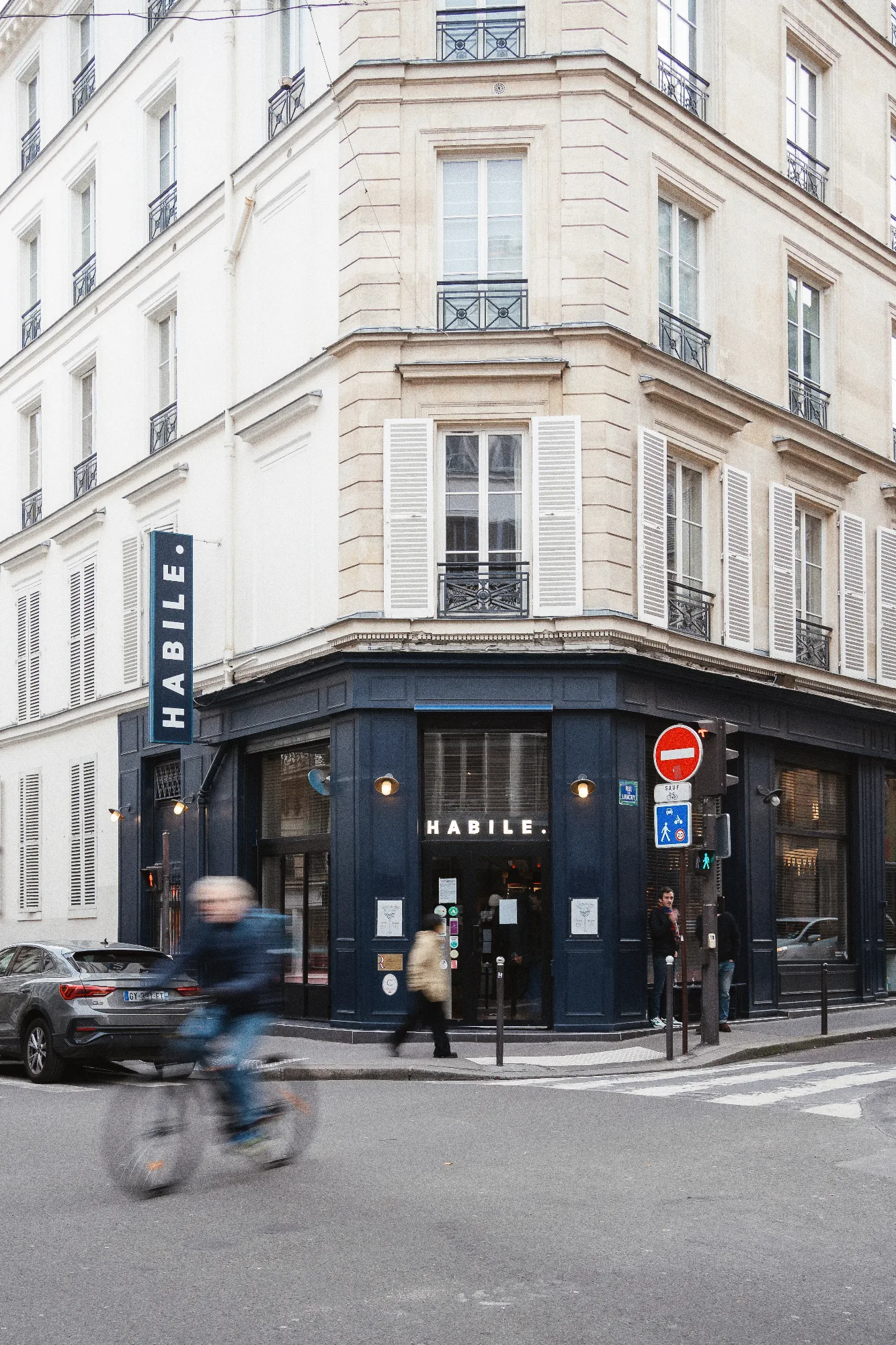 Façade d'angle d'HABILE. rue de Lancry, Paris 10 : devanture bleu nuit, enseigne lumineuse et immeuble haussmannien en pierre claire.