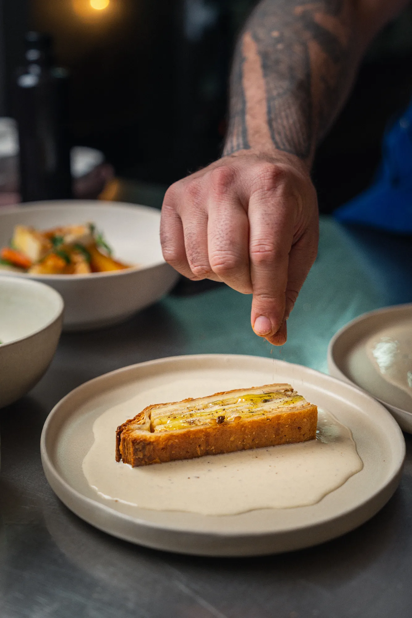 Une main assaisonne une tranche de terrine nappée de sauce crémeuse, dressée sur assiette en céramique — cuisine bistronomique à Paris 10.