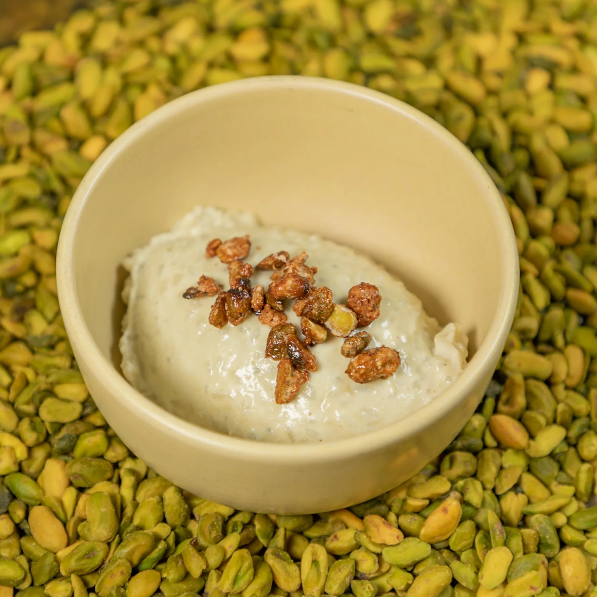 Riz au lait crémeux garni de pistaches caramélisées, posé sur un lit de pistaches décortiquées, servi au restaurant HABILE.