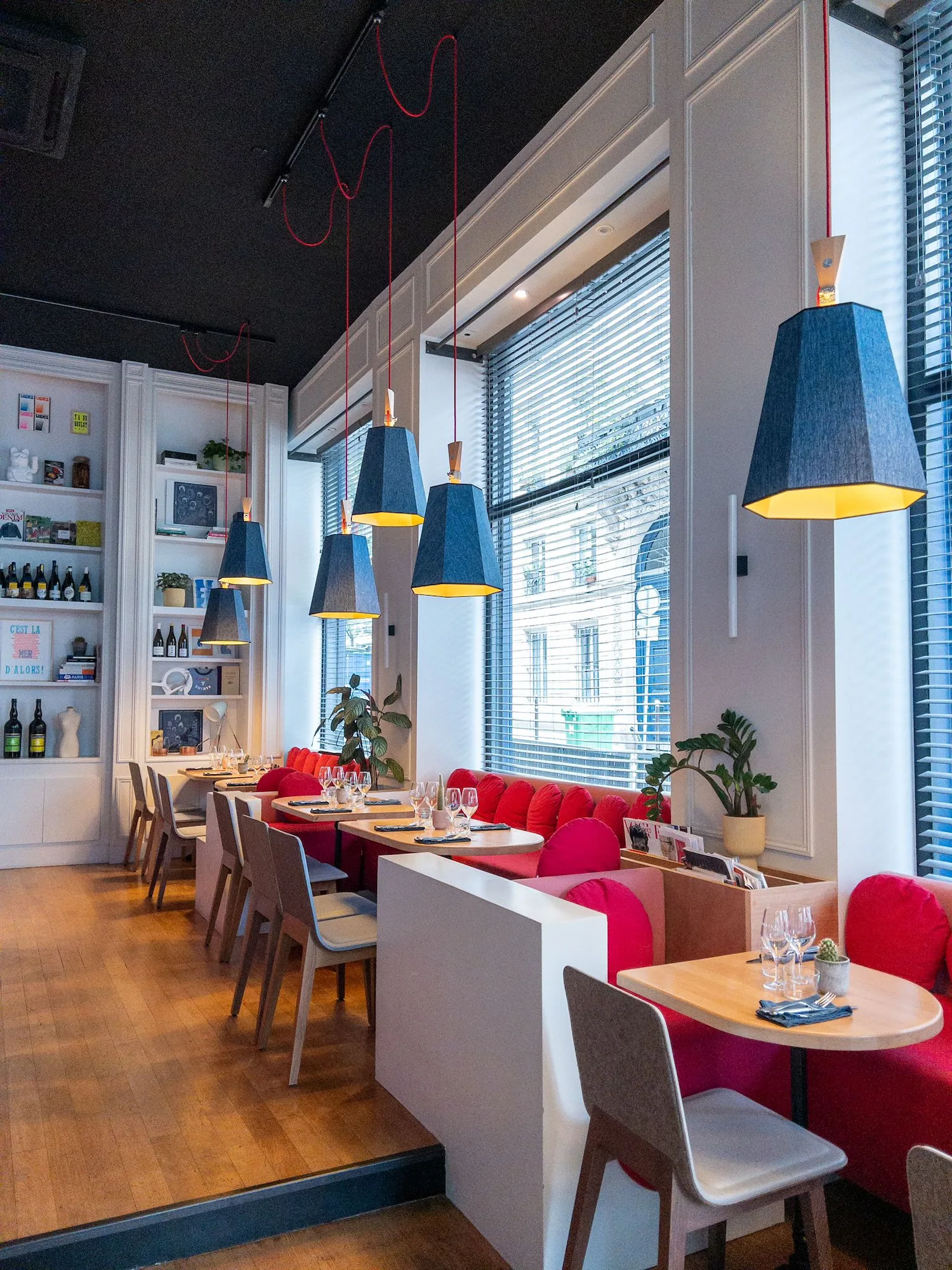 Salle du restaurant HABILE. : banquettes rouges, tables dressées, suspensions bleues à fil rouge et étagères de vins côté Paris 10.