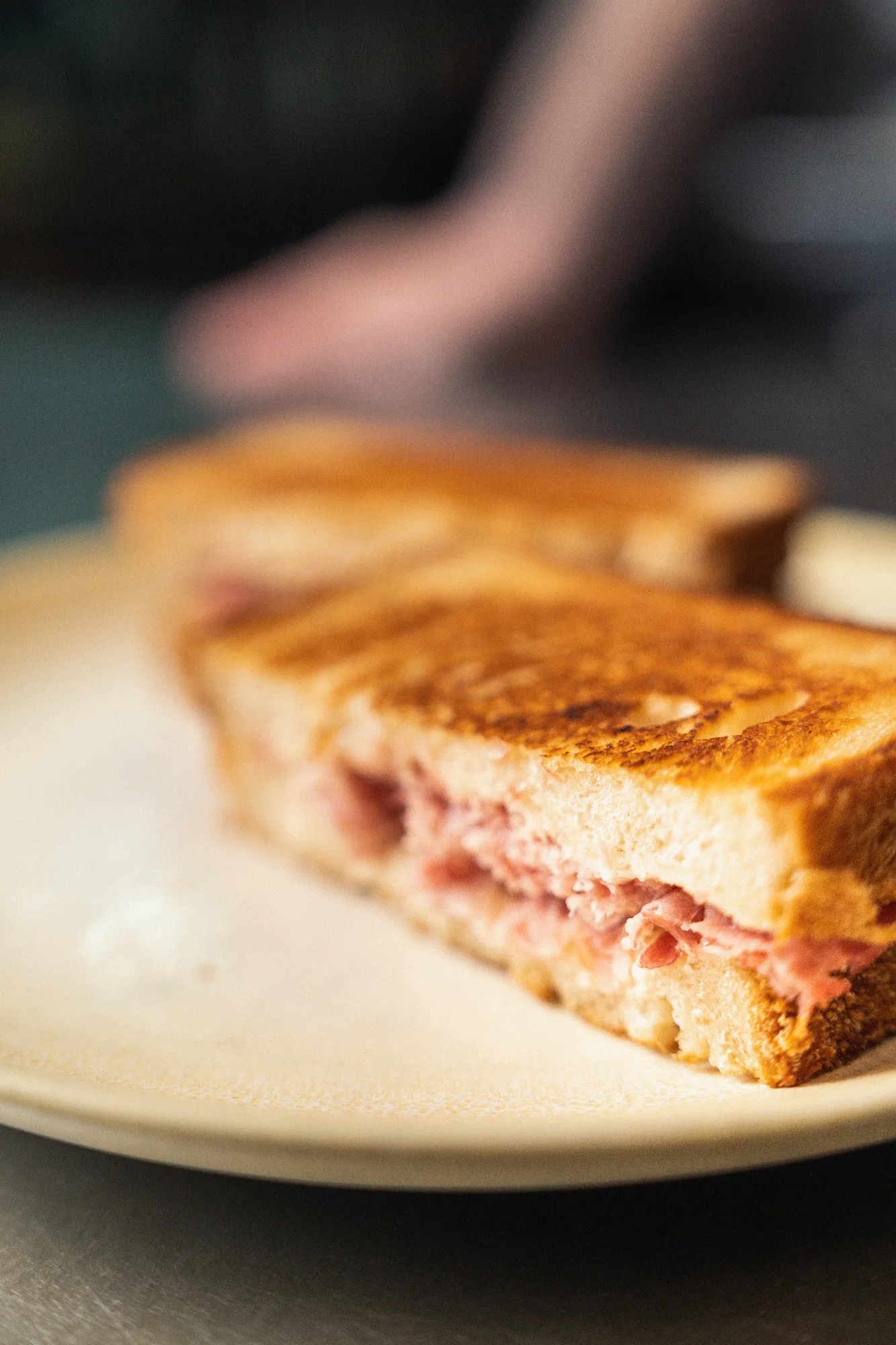 Sandwich toasté coupé en deux, garni de jambon et fromage fondu, servi sur assiette blanche au restaurant HABILE.