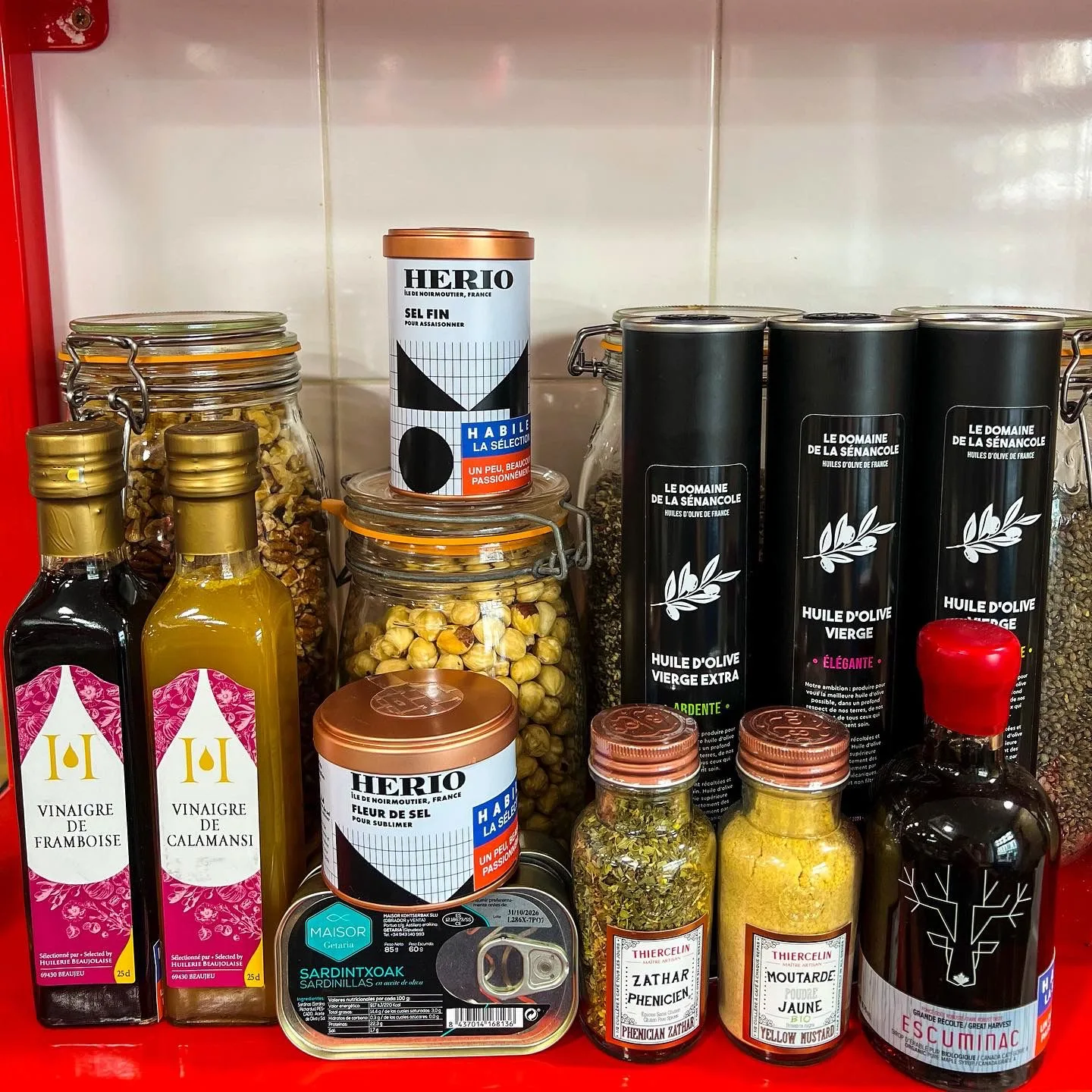 Sélection de l'épicerie fine HABILE. : huiles d'olive, vinaigres, sel de Noirmoutier, épices et conserves de sardines disposés sur une étagère rouge.