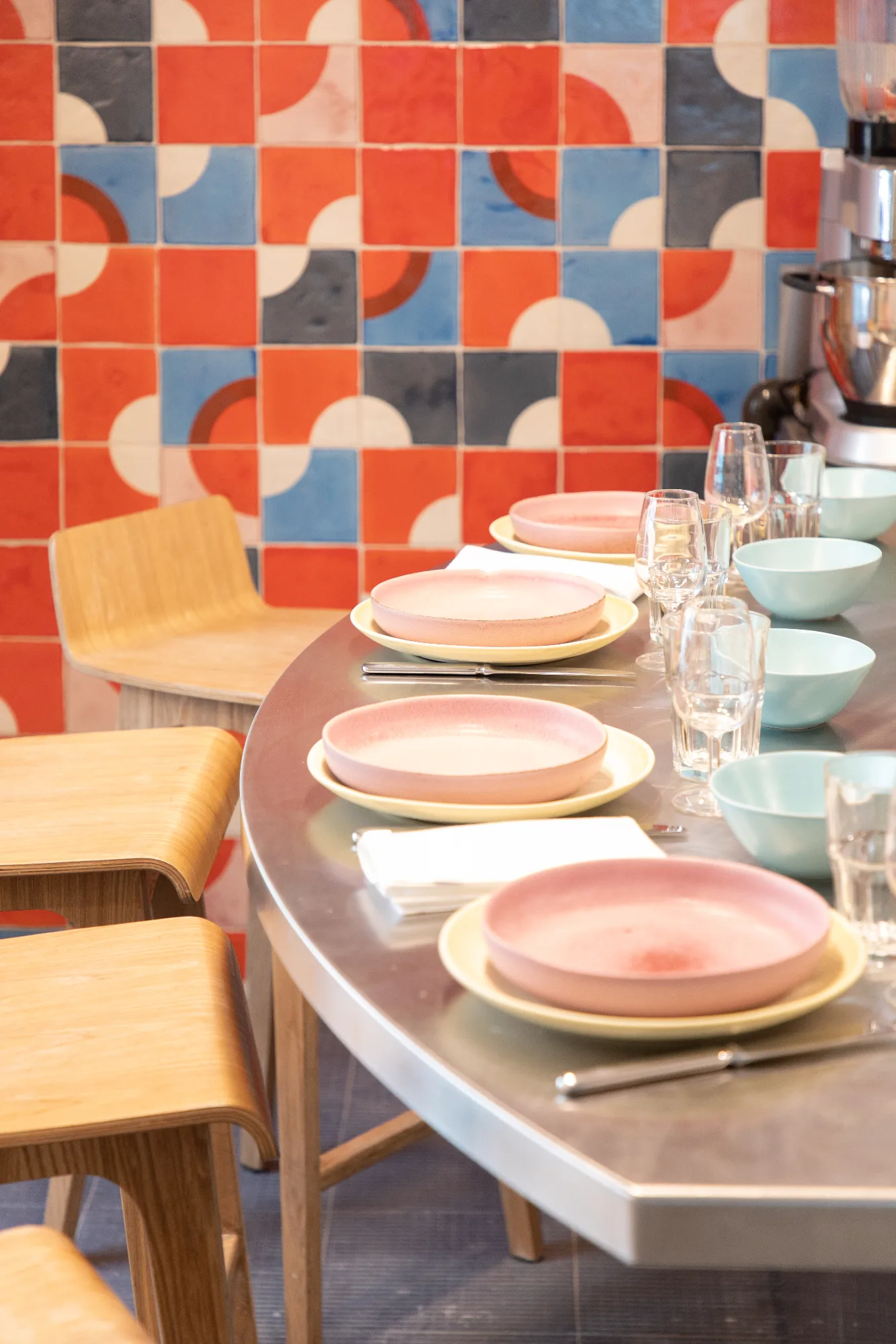 Table dressée du restaurant HABILE. : assiettes roses en céramique, bols céladon et carreaux de ciment colorés en fond de salle.