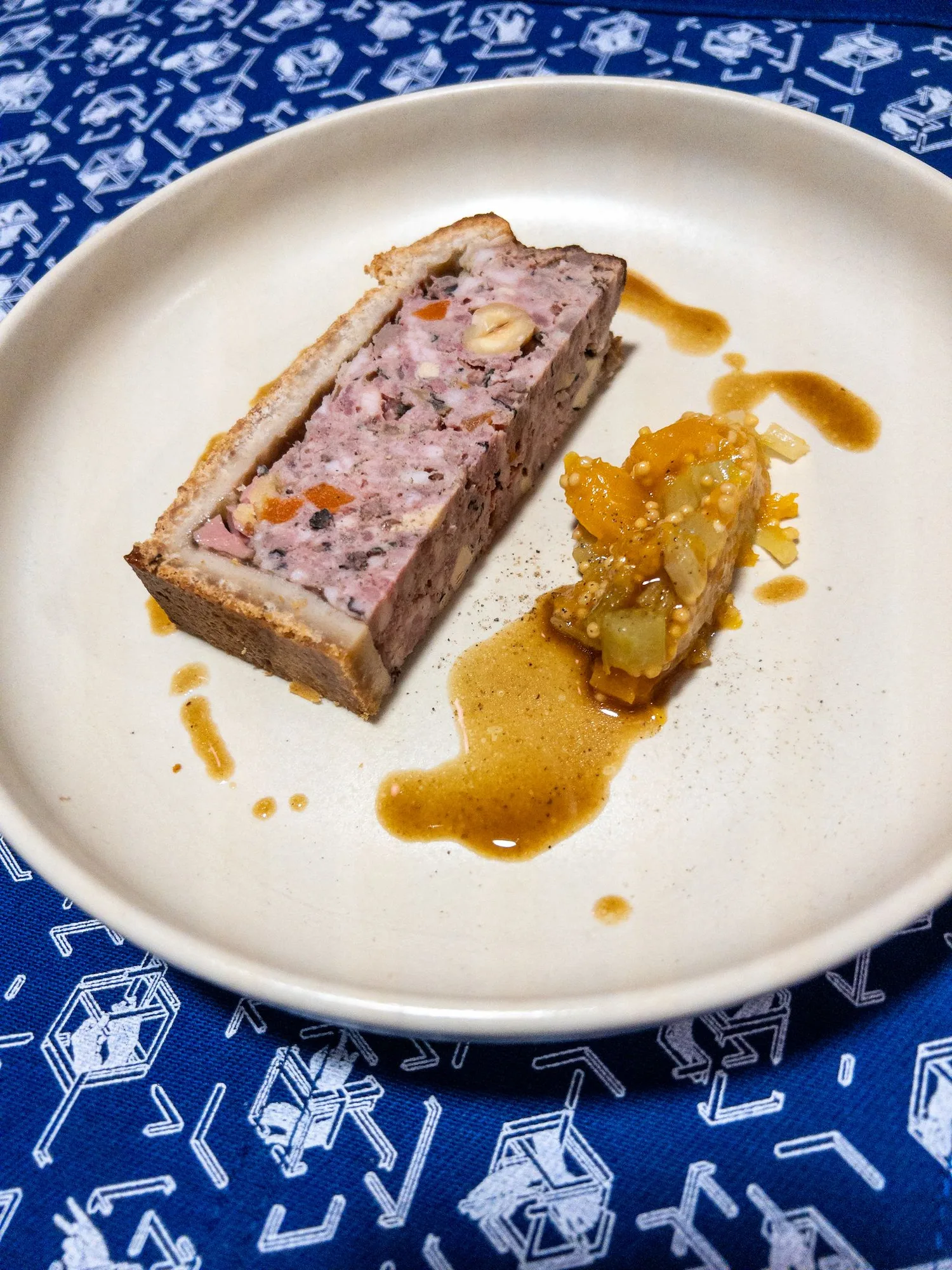 Tranche de pâté en croûte garnie, accompagnée d'un chutney fruité et d'un jus ambré, dressée sur assiette blanche — menu dégustation bistronomique.