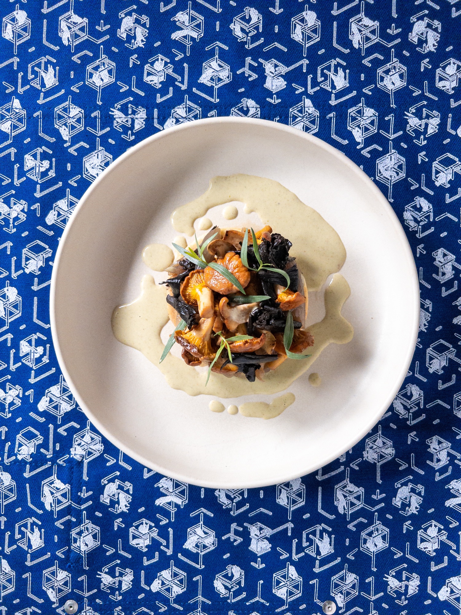 Assiette de champignons sauvages — girolles, trompettes — nappés d'une crème pâle et d'herbes fraîches, sur nappe bleue imprimée, au restaurant HABILE.