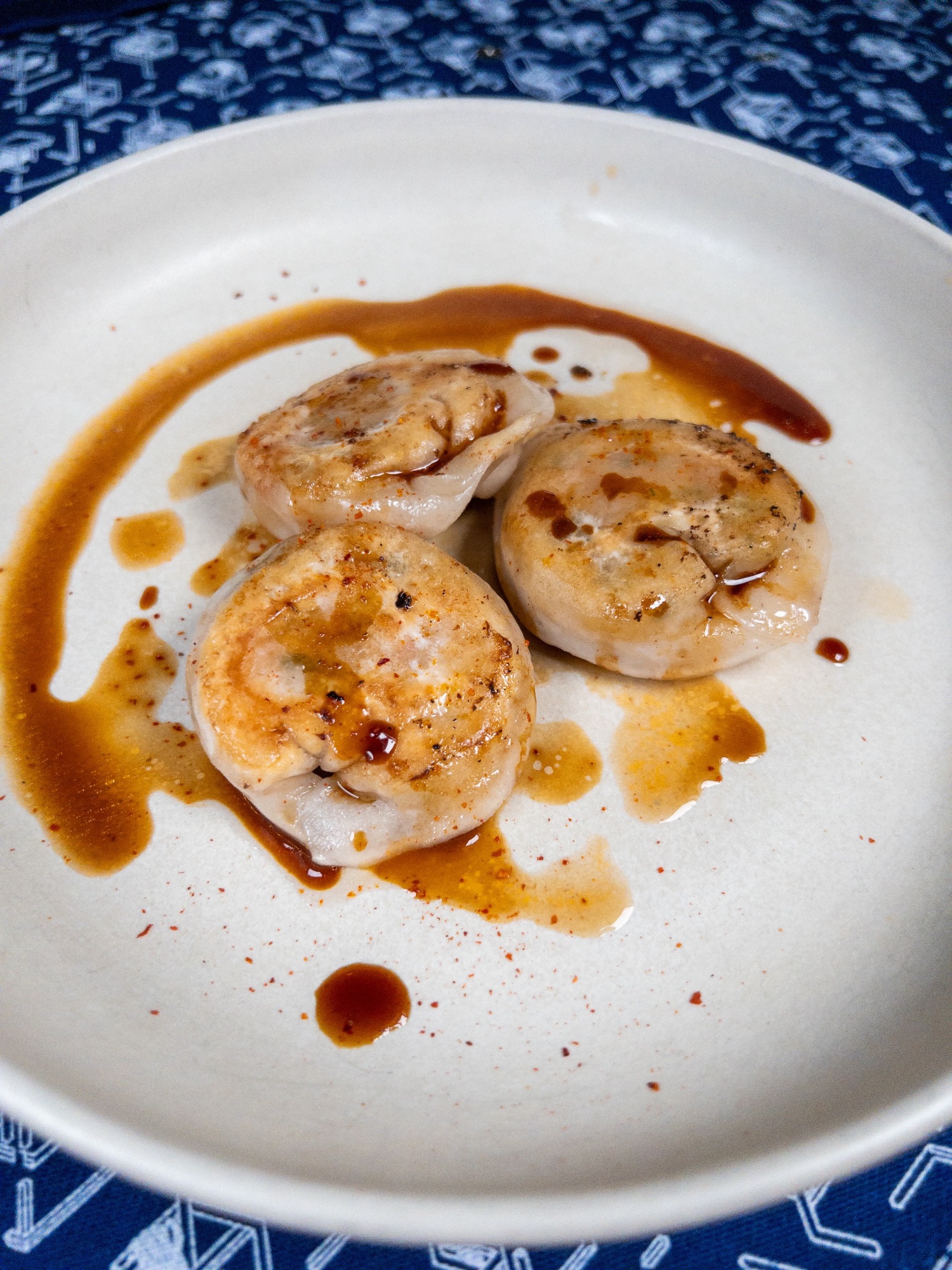 Trois gyozas de homard bleu breton à l'estragon, dorés à la poêle, nappés d'une bisque réduite sur assiette blanche, au restaurant bistronomique HABILE.