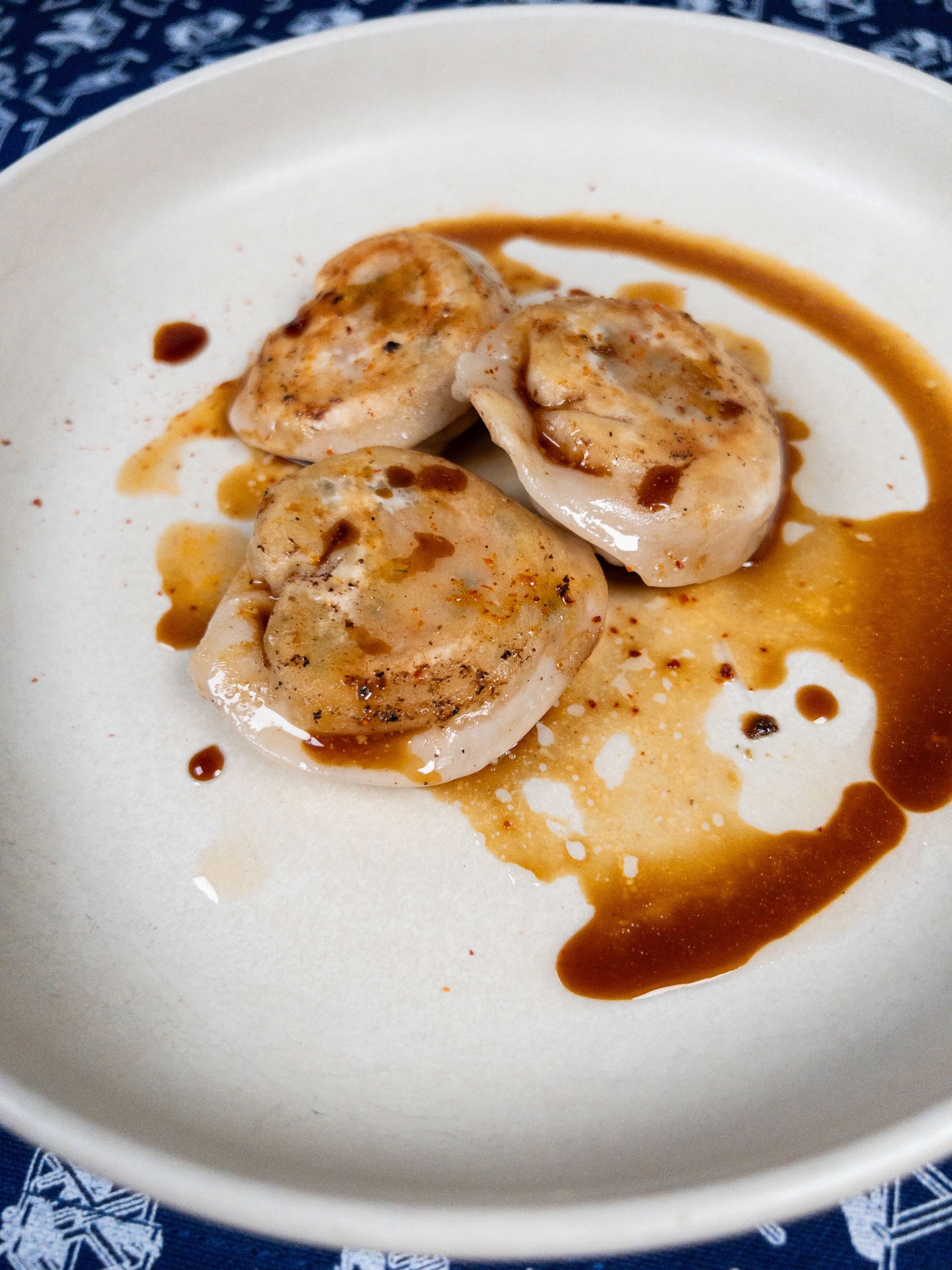 Trois gyozas de homard bleu breton à l'estragon nappés d'une bisque réduite, servis dans une assiette creuse blanche, au restaurant bistronomique HABILE.